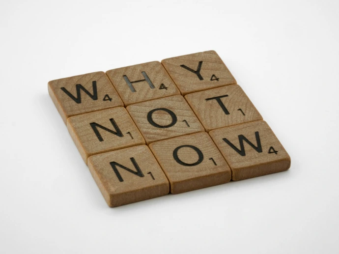 a scrabbled wooden block that says why not now